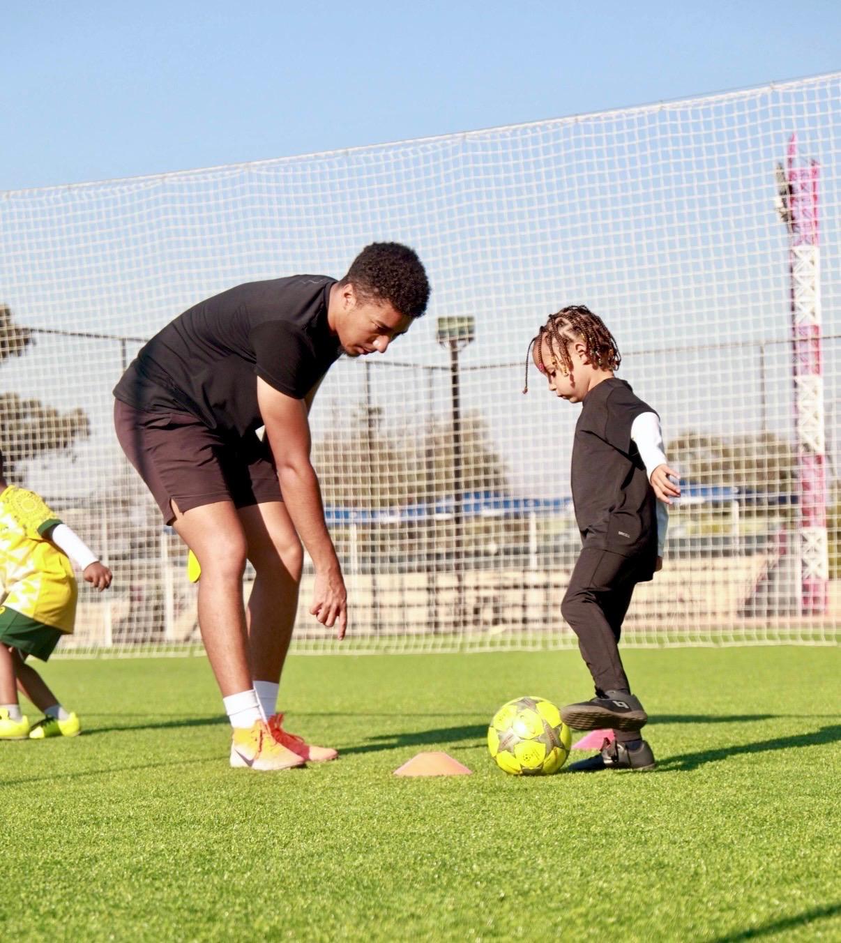 Real United coach guiding a young player during a football drill